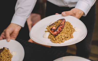 Camarero de un restaurante de lujo llevando dos platos gourmet de arroz con tentaculo de pulpo