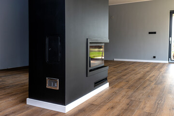 Wall Mural - A modern fireplace with a closed combustion chamber standing in the living room, painted black, with a corner pane covered with soot.