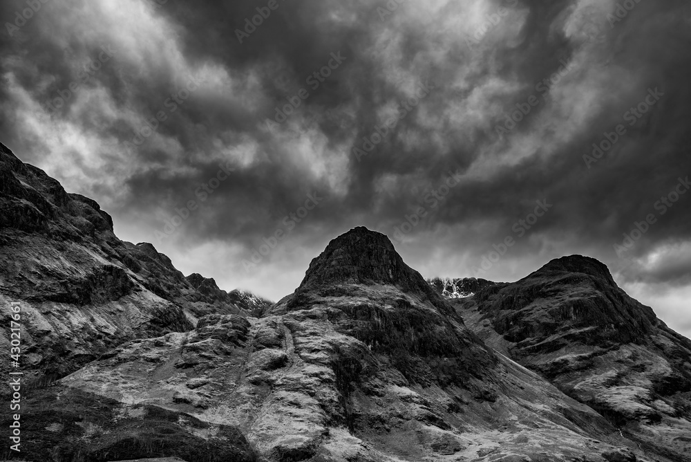 Majestic moody  black and white landscape image of Three Sisters in Glencoe in Scottish Highlands on a wet Winter day wit high water running down mountains - obrazy, fototapety, plakaty 