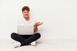 © Asier - Young caucasian man sitting on the floor holding on laptop isolated on white background holding a copy space on a palm.