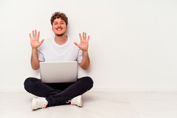 Young caucasian man sitting on the floor holding on laptop isolated on white background showing number ten with hands.