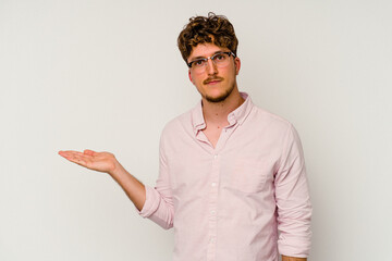 Wall Mural - Young caucasian man isolated on white background showing a copy space on a palm and holding another hand on waist.