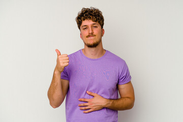 Wall Mural - Young caucasian man isolated on white background touches tummy, smiles gently, eating and satisfaction concept.