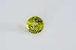 Natural green color round faceted chrysolite peridot olivine gemstone. Transparent earth mined unheated gem setting for making jewelry. White paper background. Daylight from window.