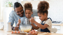 Happy Dad Teaching Two Cute Preschooler Kids To Bake. Children And Daddy Beating Eggs And Sifting Flour Into Bowl For Kneading Dough, Making Pie, Cookies Together. Family Cooking, Home Bakery Concept