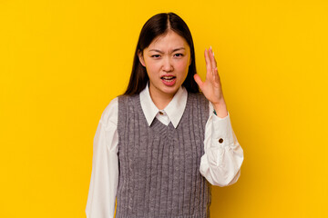 Wall Mural - Young chinese woman isolated on yellow background screaming with rage.