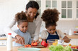 © fizkes - Happy mom teaching two preschooler kids to make vegetarian meal, slicing fresh pepper for salad. Mother and children cooking vegetables together in modern kitchen, keeping healthy eating diet