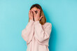© Asier - Young student caucasian woman isolated on blue background blink through fingers frightened and nervous.