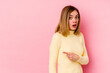 © Asier - Young caucasian woman isolated on pink background smiling and pointing aside, showing something at blank space.