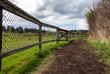 View Of A Dirt Path By A Wooden Fenced In Farm On A Cloud Filled, Sunny Day