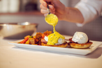 chef preparing eggs benedict with hollandaise sauce in a kitchen at a fine dining restaurant during brunch