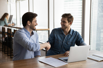 Wall Mural - Happy male employees or business partners shake hands close deal or make agreement at meeting in office. Smiling businessmen handshake get acquainted greet at briefing. Partnership concept.