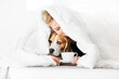 Woman morning concept. A woman lies under a blanket with her pet dog with a cup of hot drink.