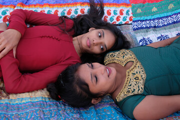 High angle shot of two female South Asian friends in traditional clothing laying down and talking