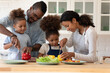 © fizkes - Happy family couple teaching two preschooler kids preparing salad. Parents and children cooking dinner together in kitchen, slicing fresh vegetables. Organic food, healthy vegetarian nutrition concept