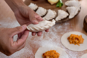 hands making the repulgue and closing of homemade Argentine empanadas and in the background empanadas finished with vegetables and filling on wooden table