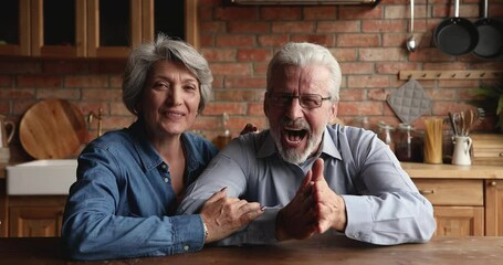 Wall Mural - Emotional happy candid older mature bonding family couple looking at camera, enjoying video call zoom online meeting with grownup children or friends, talking speaking discussing life events distantly