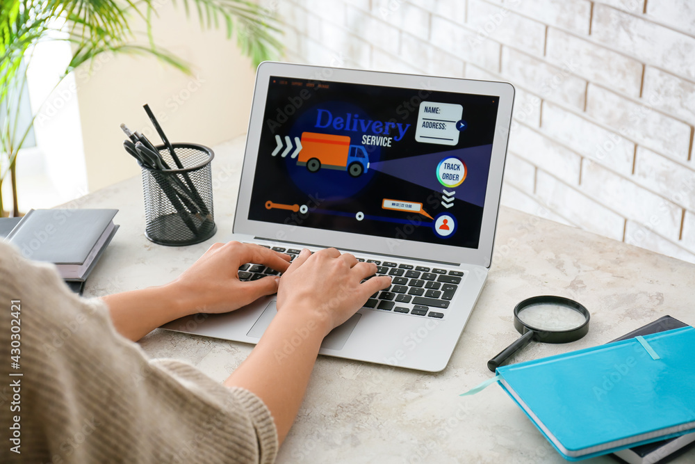 Woman using laptop with open page of delivery service application at home