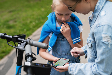Mother and daughter using application on smartphone for sharing electric scooters