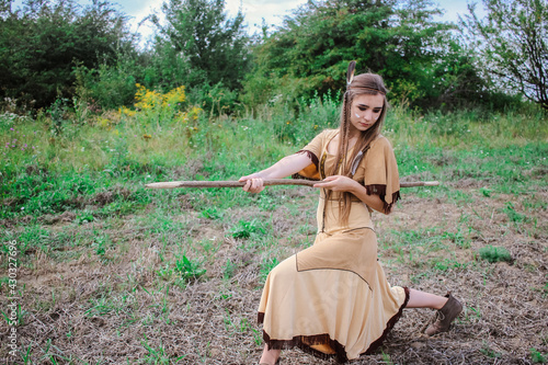 Plakat Apache tribe warrior striking with a spear, beautiful young girl in traditional dress posing in the field with a spear, confident woman scout standing with a weapon ready to attack