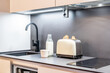 Modern black faucet in a minimal kitchen and a dishwasher. Dark stone counter table with a sink and a toaster. Healthy breakfast concept.