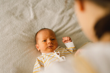 Poster - Mom dresses cute newborn little baby boy in a  jumpsuit. Happy young mother playing with baby while changing his diaper on bed.