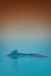 Breathtaking scenery of an island in the ocean in fog with brown and blue ombre sky above