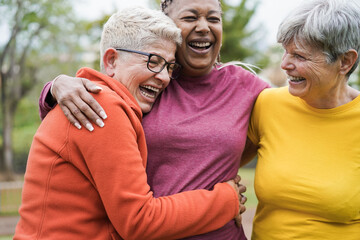 multiracial senior women having fun together hugging each others - main focus on right female face