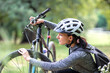 Young woman in a tracksuit checks air pressure in tire on a mountain bike in park