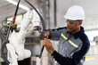 © amorn - African American male engineer worker maintenance automatic robotic arm machine in factory. Black male technician worker checking, repair automatic robot hand machine with screwdriver in smart factory
