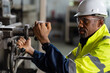 © amorn - African American male engineer worker maintenance heavy machine in the factory. Black male worker working with heavy machine with safety uniform, goggles and helmet