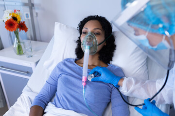 Caucasian doctor examining with stethoscope african american female patient with oxygen ventilator