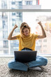 © dianagrytsku - Happy young woman sitting on a floor at home, using laptop computer, celebrating success