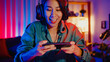© tirachard - Happy asia girl gamer wear headphone competition play video game online with smartphone colorful neon lights in living room at home. Esport streaming game online, Home quarantine activity concept.