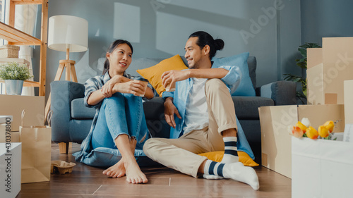 Happy asian young attractive couple man and woman sit at new home drink coffee relax and talk smile with carton package box storage to move in new house. Young married asian move home concept.