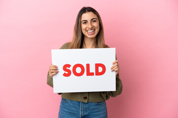 Wall Mural - Young caucasian woman isolated on pink background holding a placard with text SOLD with happy expression