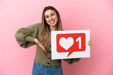 Wall Mural - Young caucasian woman isolated on pink background holding a placard with Like icon and pointing it