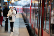 Frau mit Koffer und Maske zum Schutz vor Corona am Bahngleis im Hauptbahnhof Köln bei der Einfahrt des Zuges