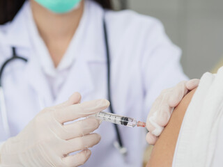 A close-up of a female doctor's hand using a syringe and cotton to vaccinate a patient, a gloved hand holding a syringe to vaccinate.