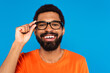 © LIGHTFIELD STUDIOS - smiling african american man adjusting glasses isolated on blue