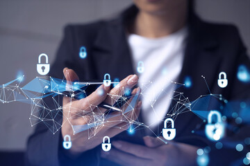 A woman programmer is browsing the Internet in smart phone to protect a cyber security from hacker attacks and save clients confidential data. Padlock Hologram icons over the typing hands. Formal wear