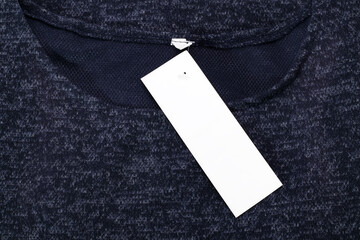 Close up of empty price tag on cloth. White rectangular clothing tag, blank label on dark blue dress.