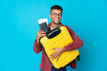 Young Brazilian man over isolated background in vacation with suitcase and passport