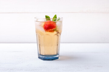 Wall Mural - a glass of iced tea with strawberries and mint on a white wooden background. soft drinks in the heat