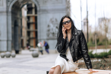 Wall Mural - Young beautiful brunette in sunglasses and fashionable outfit talking on the phone in the street