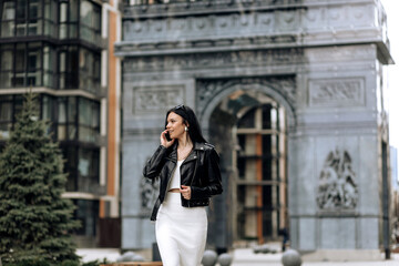 Wall Mural - Happy young business woman talking on phone while walking on the street