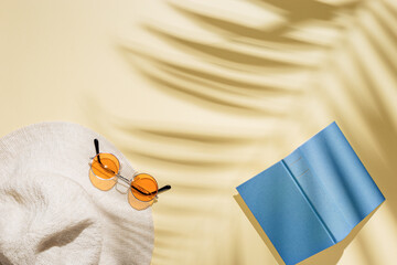 Poster - Summer minimal background with sunhat, colored sunglasses and book on sandy color background with sun shadows