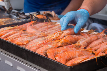 Chef cooking fresh red langoustine shrimps, prawns on grill at summer local food market - close up. Outdoor cooking, barbecue, gastronomy, seafood, cookery, street food concept