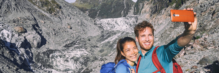 Wall Mural - Selfie couple taking phone self-portrait on New Zealand by Franz Josef Glacier. New Zealand tourists smiling happy in nature in Westland Tai Poutini National Park. Horizontal banner landscape