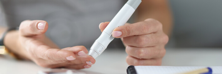 Woman holding lancet near her finger to measure blood glucose closeup